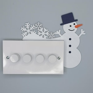May include: A white light switch cover with four round dimmer knobs, decorated with a snowman and snowflakes. The snowman has a navy blue top hat and an orange carrot nose. The snowflakes are white.