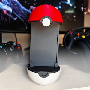 Puede incluir: Un soporte de exhibici&oacute;n vertical dise&ntilde;ado como una bola esf&eacute;rica con una mitad superior roja y una mitad inferior blanca. El centro presenta una banda negra con un bot&oacute;n circular blanco y un panel trasero rectangular negro para sostener objetos.