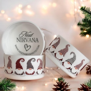 May include: Three white ceramic bowls with a gnome pattern. The bowls are decorated with red, gray, and white gnomes. The top bowl has the text "Next Nirvana" and a website address.