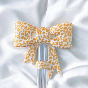 May include: A decorative bow tie with a clear, vertical support. The bow tie features a white background with a pattern of orange spots. The bow tie is made of a soft material and is suitable for various decorative purposes.