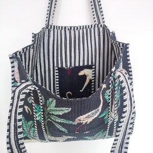 K&ouml;nnte beinhalten: Eine schwarze und wei&szlig;e gestreifte Tragetasche mit einem Blumendruck auf dem Boden. Die Tasche hat eine gro&szlig;e Tasche im Inneren und zwei lange Riemen.