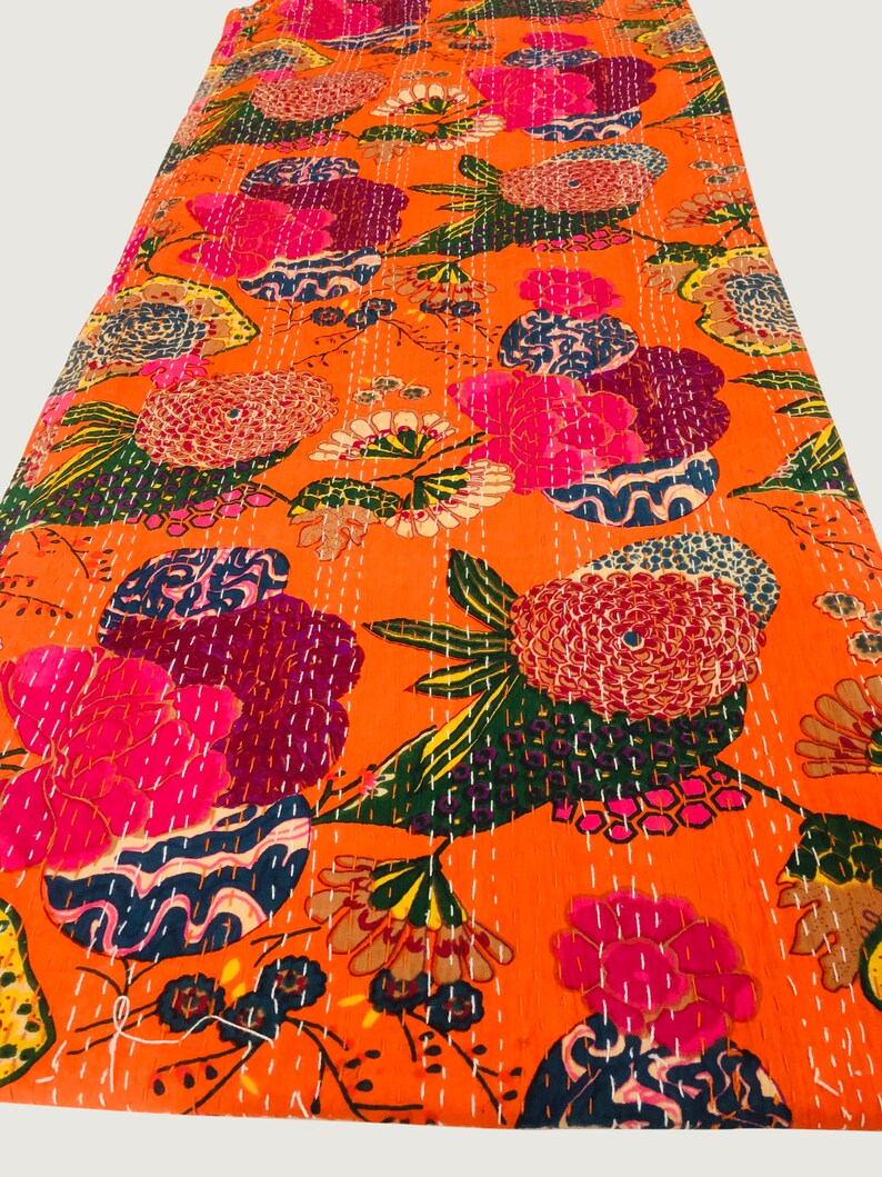 Peut inclure: Couverture kantha orange avec un motif floral dans des tons de rose, violet, bleu et vert. La couverture est cousue &agrave; la main avec du fil blanc.