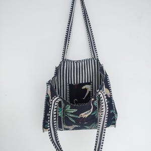 K&ouml;nnte beinhalten: Eine schwarze und wei&szlig;e gestreifte Tragetasche mit einem schwarzen und gr&uuml;nen floralen Futter. Die Tasche hat zwei lange Trageriemen und eine kleine Tasche im Inneren.