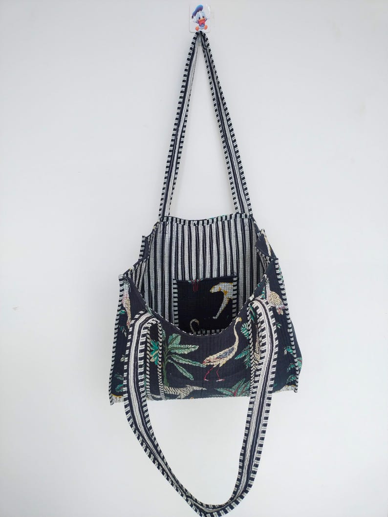 K&ouml;nnte beinhalten: Eine schwarze und wei&szlig;e gestreifte Tragetasche mit einem schwarzen und gr&uuml;nen floralen Futter. Die Tasche hat zwei lange Trageriemen und eine kleine Tasche im Inneren.