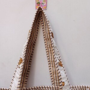 May include: A handmade tote bag with a cream background and a repeating pattern of brown stripes and small animal figures. The bag's handles are made of the same material. The bag is hanging against a white wall.