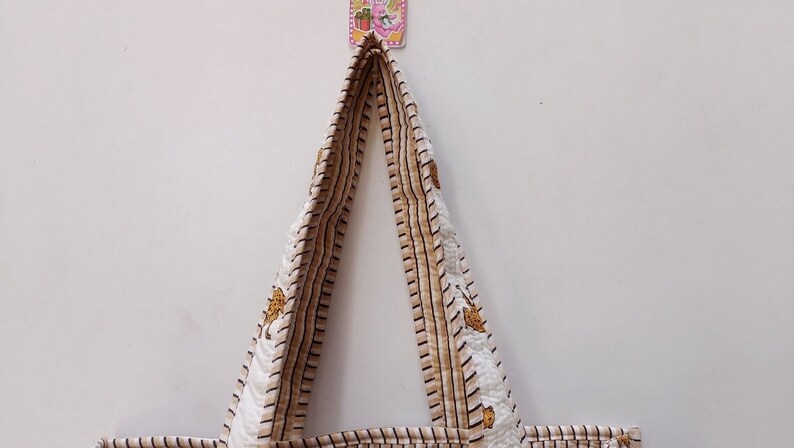May include: A handmade tote bag with a cream background and a repeating pattern of brown stripes and small animal figures. The bag's handles are made of the same material. The bag is hanging against a white wall.
