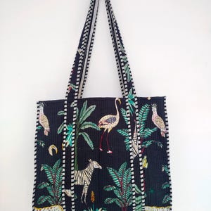 K&ouml;nnte beinhalten: Schwarze Tragetasche mit einem wei&szlig;en und gr&uuml;nen tropischen Druck mit Flamingos, Zebras und Leoparden. Die Tasche hat einen wei&szlig;en und schwarzen Besatz an den R&auml;ndern.