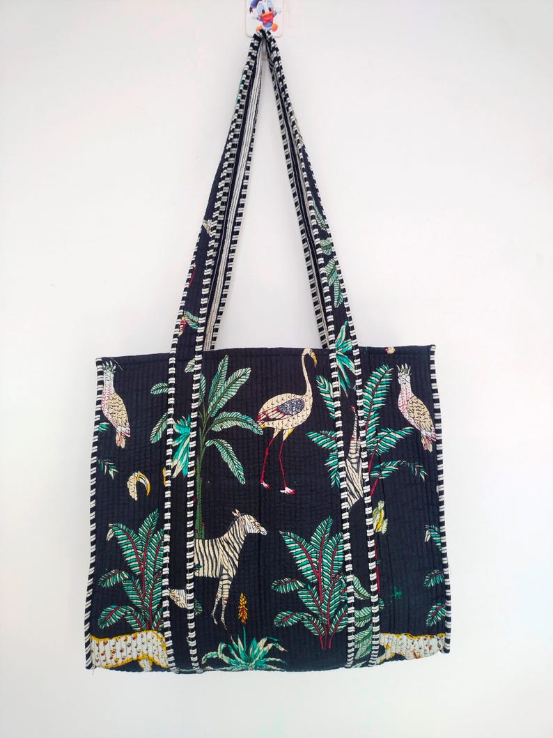 K&ouml;nnte beinhalten: Schwarze Tragetasche mit einem wei&szlig;en und gr&uuml;nen tropischen Druck mit Flamingos, Zebras und Leoparden. Die Tasche hat einen wei&szlig;en und schwarzen Besatz an den R&auml;ndern.