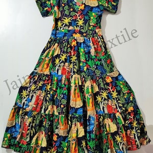 Puede incluir: Un vestido maxi de capas con mangas cortas y cuello en V. El vestido está hecho de una tela de algodón colorida con un estampado floral que presenta un patrón repetitivo de mujeres con ropa tradicional. El vestido tiene un fondo azul oscuro con colores brillantes como rojo, amarillo, verde y azul.