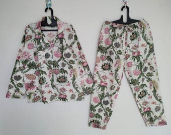 Può includere: Un pigiama bianco con stampa floreale. La parte superiore ha maniche lunghe e una chiusura con bottoni sul davanti. I pantaloni hanno una cintura con coulisse.