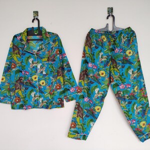 Pode incluir: Um conjunto de pijama de duas peças em azul turquesa com uma estampa floral e animal vibrante. O conjunto inclui uma camisa com botões e calças a condizer. A estampa apresenta macacos, flores e folhagens, com acabamento branco.