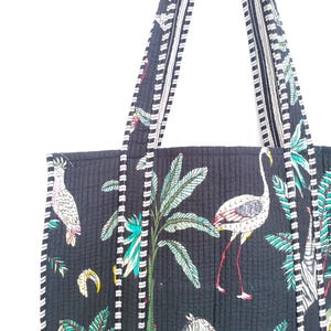 K&ouml;nnte beinhalten: Schwarze gesteppte Tragetasche mit wei&szlig;en und schwarzen Streifen an den Henkeln. Die Tasche hat einen tropischen Druck mit Palmen, Flamingos und Zebras.