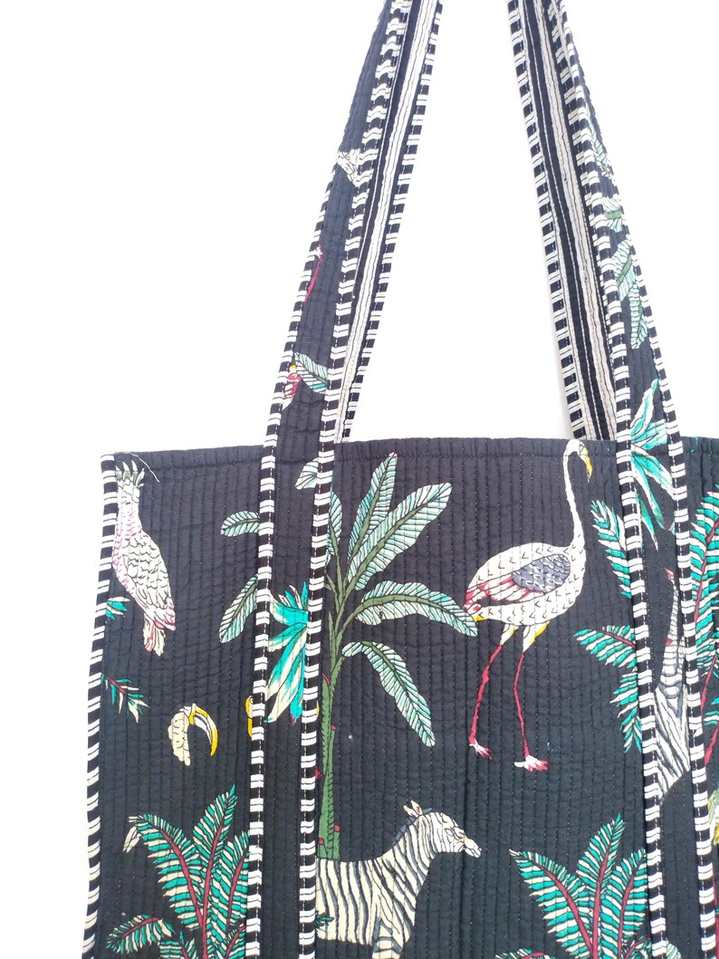 K&ouml;nnte beinhalten: Schwarze gesteppte Tragetasche mit wei&szlig;en und schwarzen Streifen an den Henkeln. Die Tasche hat einen tropischen Druck mit Palmen, Flamingos und Zebras.