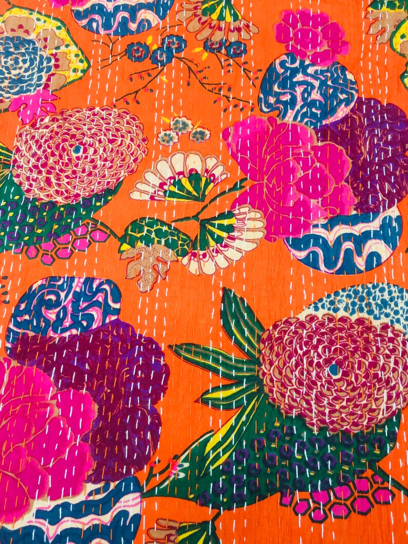 Peut inclure: Un tissu orange vif avec un motif floral. Les fleurs sont roses, violettes, bleues et vertes. Le tissu est matelass&eacute; avec du fil blanc.