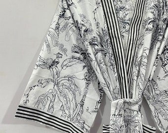 Könnte beinhalten: Eine weiße Baumwollrobe mit einem schwarz-weißen tropischen Muster. Die Robe hat einen schwarz-weißen Streifenbesatz und einen Bindegürtel.