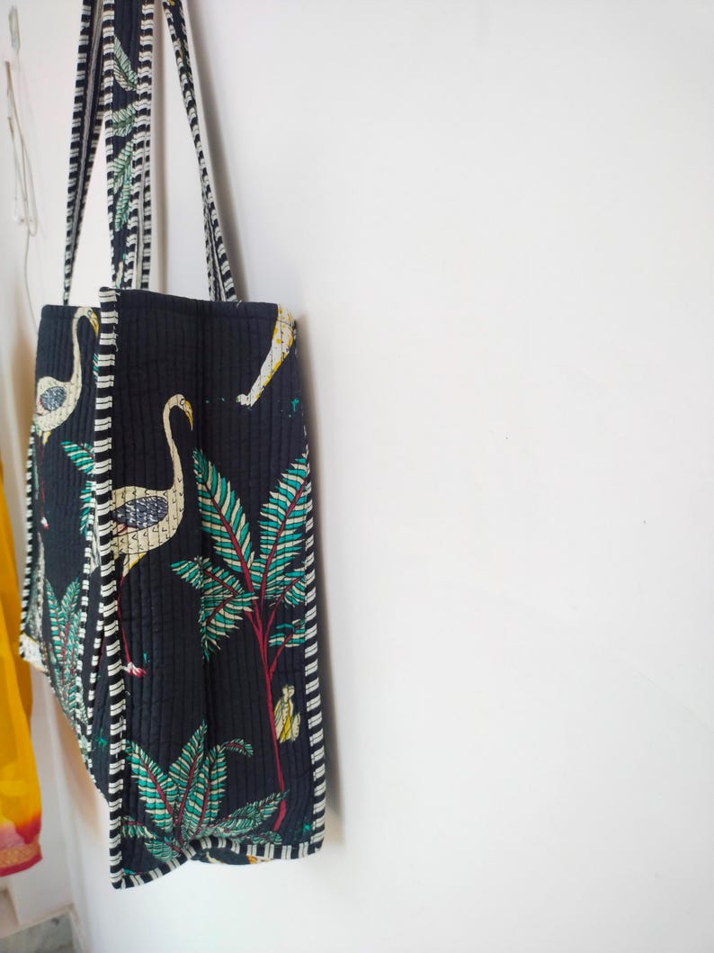 K&ouml;nnte beinhalten: Eine schwarze gesteppte Tragetasche mit wei&szlig;-schwarzem Besatz. Die Tasche hat einen floralen und Vogel-Druck in Gr&uuml;n-, Wei&szlig;- und Gelbt&ouml;nen.