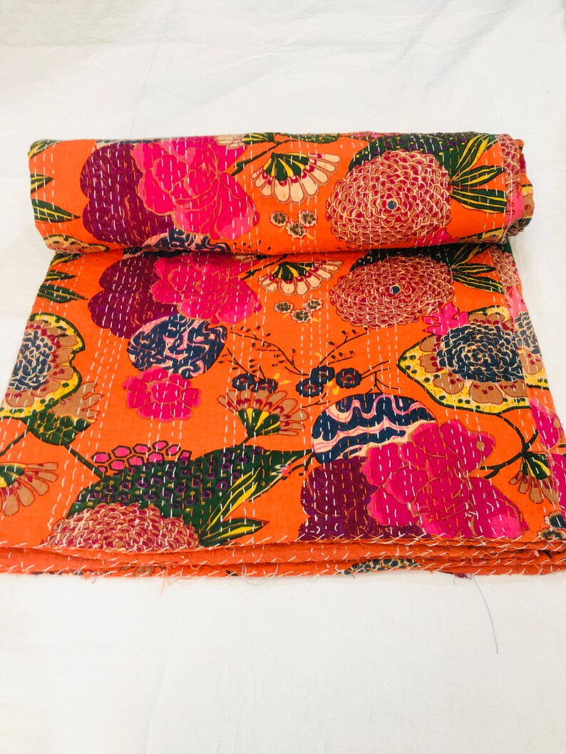 Peut inclure: Une courtepointe kantha orange vif avec un motif floral dans des tons de rose, violet, vert et jaune. La courtepointe est pli&eacute;e en trois et a un fond blanc.