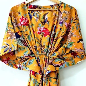 May include: A yellow kaftan with a floral print featuring birds and flowers. The kaftan has a V-neck and short sleeves.
