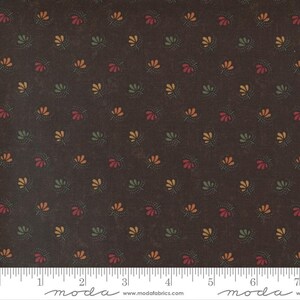 May include: Dark brown fabric with a repeating pattern of small, stylized floral designs in red, green, and yellow. The fabric has a slightly distressed appearance, with a ruler along the bottom edge.