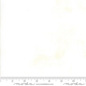 May include: White fabric with subtle yellow-green shading. A ruler is printed along the bottom edge, with the word "moda" and the website address www.modafabrics.com printed below the ruler.