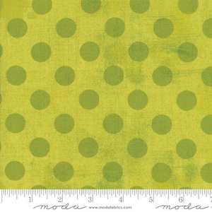 May include: Close-up of a fabric with a repeating pattern of large, olive green polka dots on a bright yellow-green background. The fabric has a textured appearance. A ruler is at the bottom of the image.