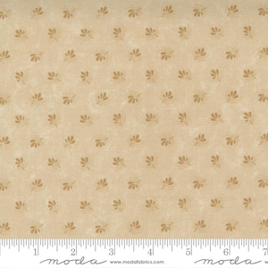 May include: Tan fabric with a repeating pattern of small, stylized floral designs in a darker shade of tan. The fabric has a slightly mottled appearance, and a ruler is visible along the bottom edge.