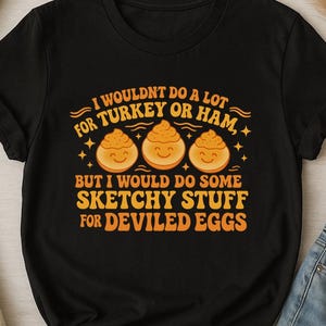 May include: Black t-shirt with the text "I wouldn't do a lot for turkey or ham, but I would do some sketchy stuff for deviled eggs." The design includes three smiling deviled egg illustrations.