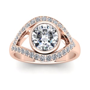 May include: A rose gold ring with a large round diamond set in a bezel setting. The diamond is surrounded by a halo of smaller diamonds. The ring is designed in the shape of an eye.