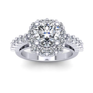Puede incluir: Un anillo de compromiso de plata con un gran diamante redondo central rodeado por un doble halo de diamantes más pequeños. La banda está adornada con diamantes más pequeños a cada lado.
