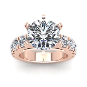 May include: A rose gold engagement ring with a large round center diamond and smaller diamonds set in a pave band.