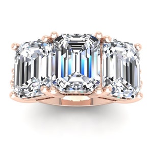 Puede incluir: Un anillo de compromiso de tres piedras con diamantes de talla esmeralda engastados en una banda de oro rosa.