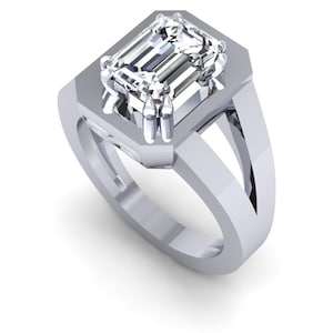 May include: A silver ring with a large, clear emerald-cut diamond set in a square bezel. The ring has a thick band with a split shank.