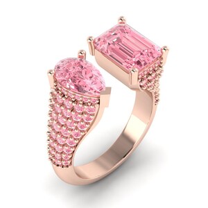 Puede incluir: Un anillo de oro rosa con dos piedras rosas. Una es de talla esmeralda y la otra en forma de pera. El anillo está adornado con piedras rosas más pequeñas a lo largo de la banda. Diseño moderno y elegante.