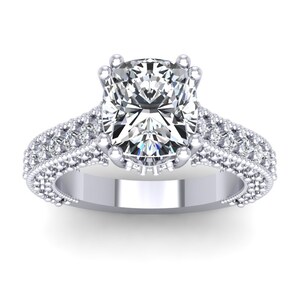 May include: A silver engagement ring with a large, cushion-cut diamond center stone. The band is adorned with smaller diamonds set in a pave setting.