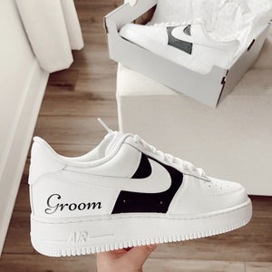 May include: White leather trainers with a black swoosh and the word "Groom" written on the side. The trainers have a white sole with a black "Air" logo.