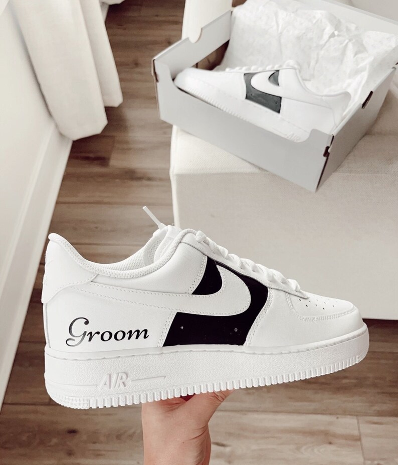 May include: White leather trainers with a black swoosh and the word "Groom" written on the side. The trainers have a white sole with a black "Air" logo.