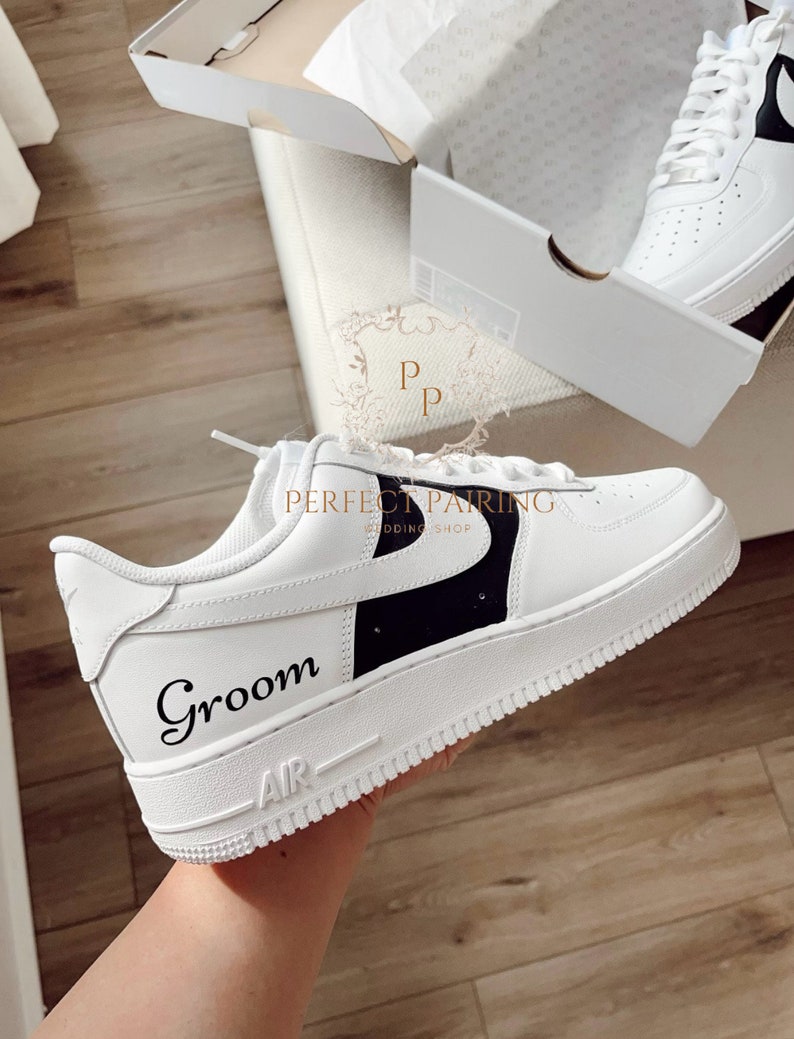 May include: White leather trainers with a black swoosh and the word "Groom" written in black script. The trainers have a white sole with black trim.