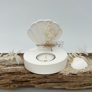 Könnte beinhalten: Weißer Kerzenhalter aus Keramik in Muschelform mit einer kleinen weißen Kerze und getrockneten weißen Blumen. Der Halter steht auf einem Stück Treibholz mit einer kleinen weißen Muschel. Der Text "Ahoy" steht auf einem kleinen weißen Etikett.