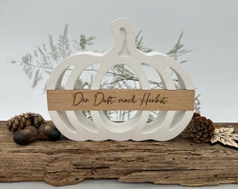 May include: White wooden pumpkin cutout with a wood sign that reads "Der Duft nach Herbst". The pumpkin is sitting on a piece of driftwood.