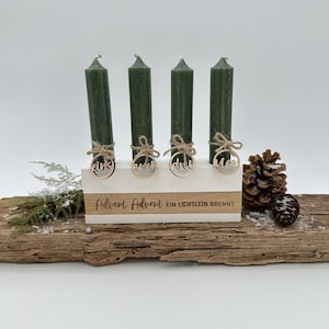 Könnte beinhalten: Ein Holz-Adventskranz mit vier grünen Kerzen. Der Kranz hat eine weiße Basis mit dem Text "Advent Advent Ein Lichtlein Brennt" und vier Holz-Kreise mit den Zahlen "eins", "zwei", "drei" und "vier" darauf.