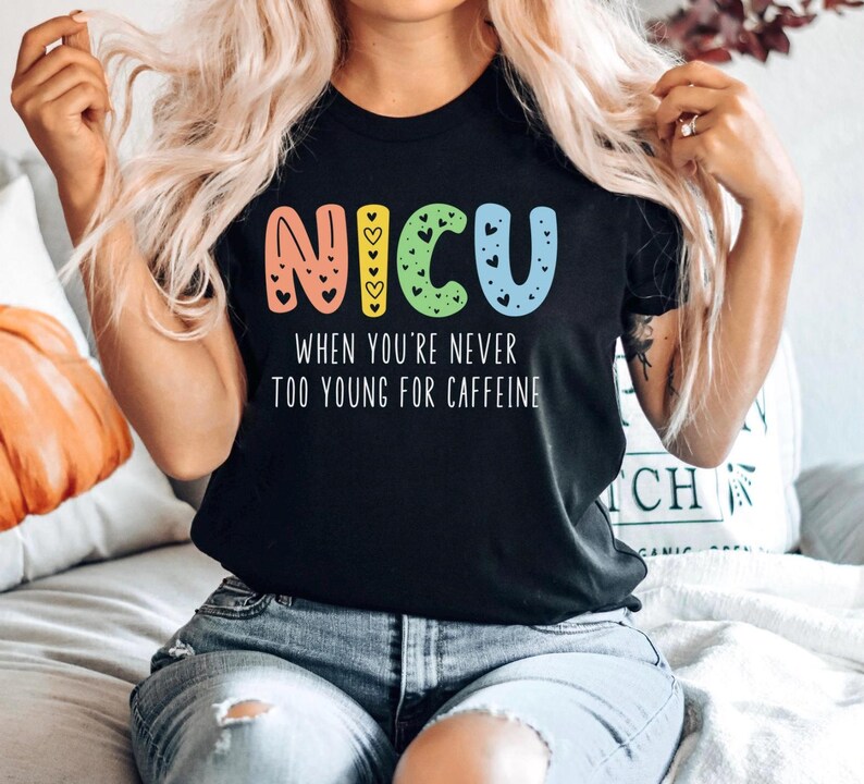 May include: Black t-shirt with a colorful "NICU" graphic and the text "When you're never too young for caffeine".