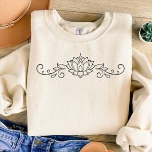 May include: A cream colored sweatshirt with a black lotus flower and floral design on the front.
