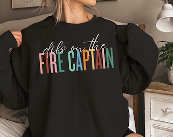 May include: Black sweatshirt with the text "dibs on the FIRE CAPTAIN" in rainbow colors.