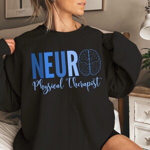Puede incluir: Sudadera negra con las palabras "NEURO Physical Therapist" en azul. Un gr&aacute;fico de cerebro azul est&aacute; a la derecha de la palabra "NEURO". El texto est&aacute; en una fuente sans-serif, con "Physical Therapist" en una fuente cursiva.