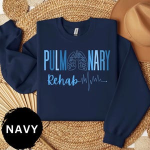 May include: Navy blue sweatshirt with the words "PULMONARY Rehab" in blue, along with a lung graphic and a heartbeat line. The word "NAVY" is in a black circle in the lower left corner.