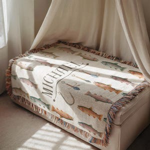 May include: Cream-colored throw blanket featuring a repeating pattern of colorful fish. The blanket has a fringed edge with a mix of colors. The name "MICHAEL" is printed in a decorative font, along with fishing-related illustrations.