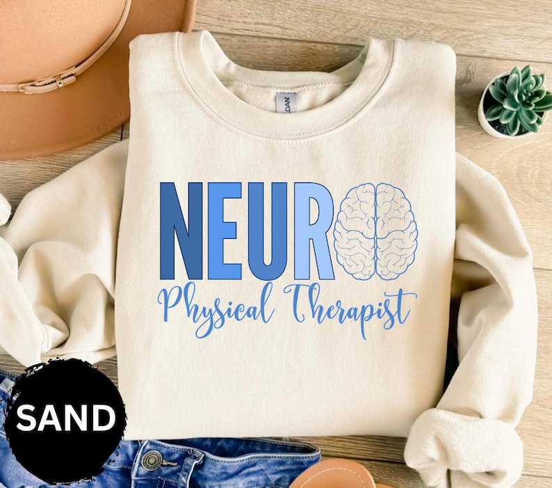 Puede incluir: Sudadera color arena con la palabra "NEURO" en letras azules, un gr&aacute;fico de cerebro y las palabras "Physical Therapist" en cursiva. La sudadera es de cuello redondo.