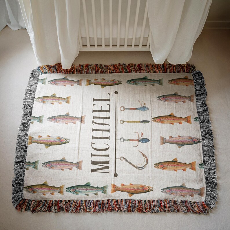 May include: Cream-colored woven throw blanket featuring a pattern of colorful fish and fishing lures. The name "MICHAEL" is printed vertically in black. The blanket has a fringed edge in shades of red, brown, and gray.