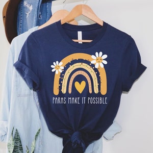 May include: A navy blue t-shirt with a rainbow design featuring a yellow heart and daisies. The text "Paras make it possible" is printed on the shirt.