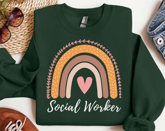 May include: A dark green sweatshirt with a rainbow design and the text "Social Worker". The rainbow is made up of orange, brown, and pink stripes with white polka dots. A pink heart is in the center of the rainbow.
